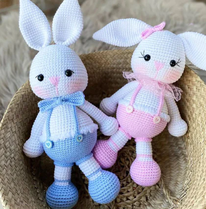 Hasır sepette mavi ve pembe tulumlu, tığ işiyle örülmüş iki amigurumi tavşan